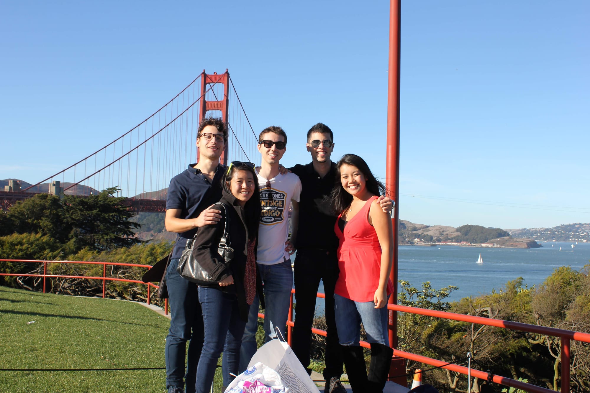 A group photo of five young professionals smiling in front of the Golden Gate Bridge in San Francisco on a sunny day, with the iconic red bridge and bay in the background.